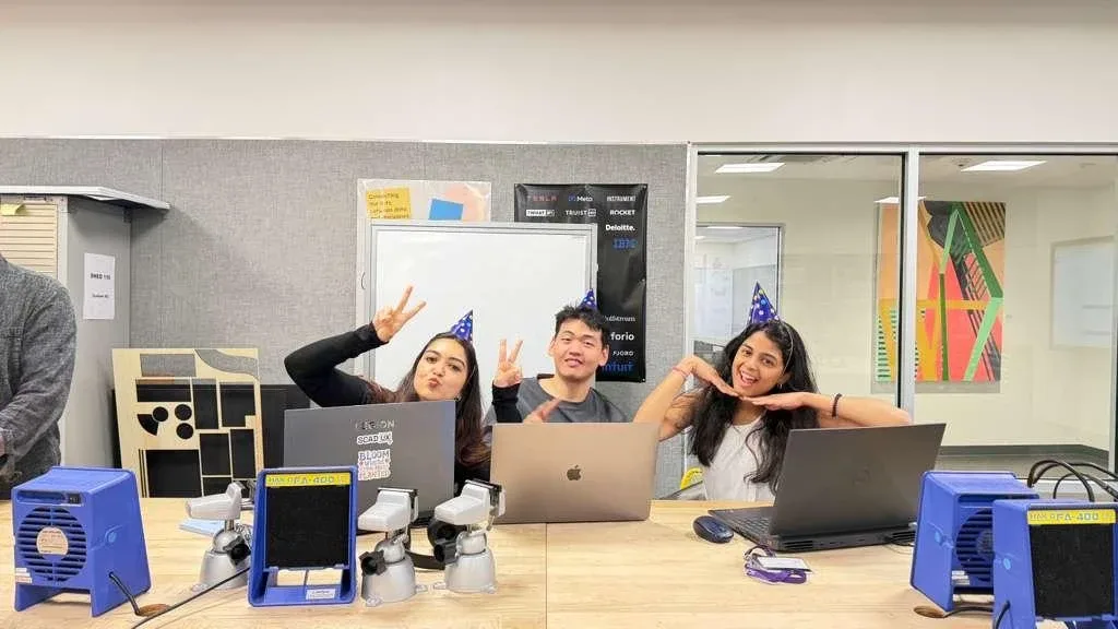 Navyaa and teammates in party hats at their laptops.